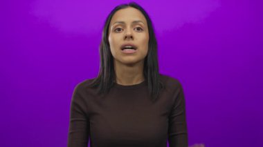 Canlı mor bir duvarın önünde şaşkınlığını ifade eden bir kadın, elleri yüzünü çerçeveliyor, şaşkınlık hissini vurguluyor ve koyu renk arkaplan ile kontrastı.