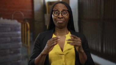 Gözlüklü bir kadın bir inşaat alanında sarı bluz giyerek şaşkınlık ve kararlılık gösteriyor. Duygularını ve güvenini gösteriyor.