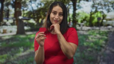 Genç İspanyol kadın kırmızı bir keçeli kalp tutuyor ve bir orman açıklığında dururken çenesine dokunuyor; dingin yansıma.