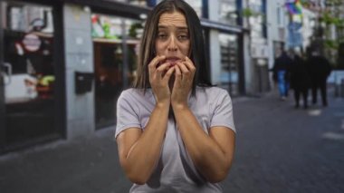 Şehir caddesinde tırnaklarını yiyen kadın, elleri gergin ve ileri; endişe belirsizliği.