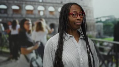 Kolezyumun dışında duran bir kadın, Roma 'da gözlük takıyor ve uzun saçlı çizgili bir gömlek giyiyor, arka planda insanlarla çevrili, samimi bir anı yakalıyor..