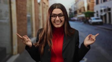 Sokakta gülümseyen bir kadın, iki eli gözlüklü ve kırmızı gömlekli, şehir ortamında, tercihini veya yönünü ima ediyor..