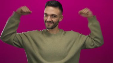 Cesur pembe bir arka plana karşı kaslarını kasan genç adam, mutluluk ve güç gösterisi yapıyor..