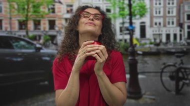 Kırmızı tişörtlü bir kadın elinde kırmızı kahve fincanı tutarken iki elini de bisiklet dolu bir şehir sokağına koydu. Huzur, huzur, huzur ve sükunet..