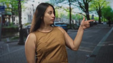 Kadın, park halindeki arabaların ve sokak lambalarının yakınındaki ağaçlar boyunca iki parmağını da sağa doğru gösteriyor..