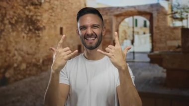 İspanyol adam gülümsüyor ve taştan bir jest yapıyor. Eski bir kasabanın şehir sokağında neşeli bir ifade ve kırsal mimari geçmişi olan enerjik bir gençlik enerjisi sergiliyor..