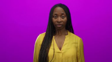 Sarı bluzlu kadın canlı pembe arka planda duruyor. Uzun örgüleri ve sakin ifadesiyle izole stüdyo ortamında kendine güveni tam bir güzellik ve tarz sergiliyor.