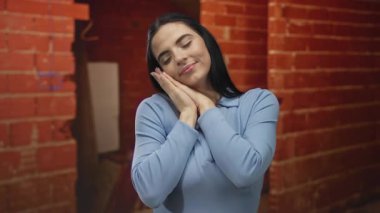 Mavi gömlekli İspanyol kadın uyukluyor ve kırmızı tuğladan duvarları olan kapalı inşaat alanında geriniyor, bitmemiş bir ortamda rahat bir anı yakalıyor..