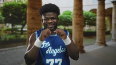 Sokak sütununda bilekliklerle gözlerini ovuşturan adam mavi Los Angeles basketbol forması giyiyor..