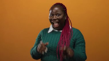 İzole edilmiş turuncu bir arka plan karşısında gülümseyen ve kameraya işaret eden kadın neşeli ve renkli bir ortamda mutluluk ve kendine güveni ifade ediyor..