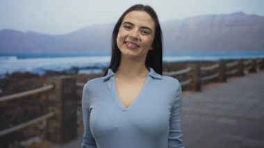 Okyanus kıyısındaki mavi gökyüzünün altında yüzünü örten ve ortaya çıkaran genç bir kadın neşeyle gülümsüyor.