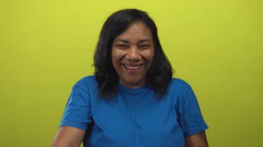 Afro-Amerikalı kadın kamerayı işaret ediyor ve limon yeşili stüdyoda geniş bir gülümseme sergiliyor; neşe dolu kahkahalar mutluluk eğlencesi.
