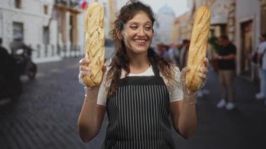 Bir kaldırım taşı caddesinde elinde iki baget tutan kadın çizgili önlük ve plastik eldiven giyiyor; sıcak bir konukseverlik..