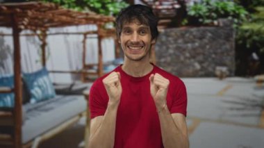 Adamın biri göğüs göğüse yumruklar kaldırıyor ve açık alanda taş duvarlı binaya gülümsüyor. Zafer sevinci..