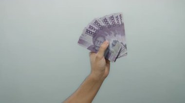 Endonezya rupia banknotları tutan adamın eli izole edilmiş beyaz bir arka plan, çeşitli mali bağlamdaki para birimlerini gösteriyor.
