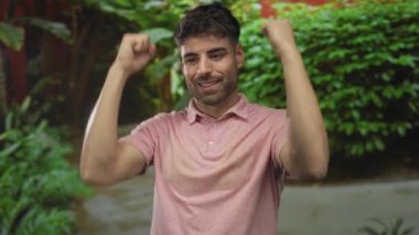 Pembe tişörtlü genç İspanyol adam sıkılmış yumruklarını ve çıplak kollarını yemyeşil orman yolunda kaldırıyor; güven zaferi.