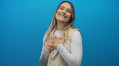 Mavi izole edilmiş arka plana karşı kollarını açmış gülümseyen kadın mutluluk ve sıcaklık yayıyor, pozitiflik, neşe ve dostça selamlaşma kavramları için ideal..