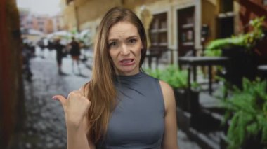 Kolsuz üst baş giyen kadın tiksindirici yüz ifadesiyle başparmağıyla şehir caddesine gidiyor..