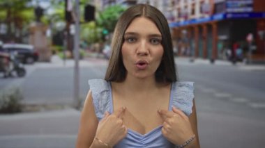 Genç beyaz kız yaz öğleden sonra şehir caddesinde yoğun bir trafik varken parmak göğse göğüs dekoltesini işaret ediyor..