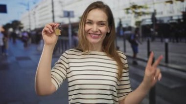 Yoğun şehir caddesinde ev anahtarlığı ve parlak bir gülümseme tutan genç kadın, ev sahipliği mutluluğu.