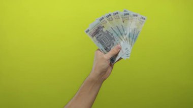 Parlak sarı arka plana karşı izole edilmiş Romen banknotlarını elinde tutan beyaz adam, canlı bir ortam yoluyla finans ve ekonomik kavramları vurguluyor.