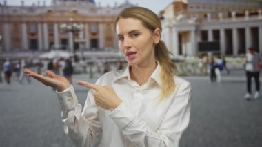 St. Peter Meydanı, Vatikan 'da elinde ok işareti olan, beyaz gömlekli, açık havada gezen genç sarışın kadın avucunun sembolik bir konumda olduğunu gösteriyor.