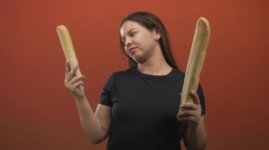 Stüdyoda iki baget tutan kadın sol ve sağ somunu, elini kaldırarak turuncu arka planla karşılaştırıyor. Kararsızlık..