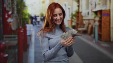 Canlı bir şehir caddesinde elinde İsveç banknotları tutan, neşeli bir ifade sergileyen ve açık bir şehir ortamında para birimini ön plana çıkaran bir kadın..