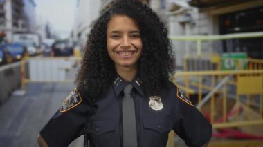 Üniformalı bir kadın bir inşaat alanında gülümsüyor, şehir ortamında kendine güveni tam bir varlık sergiliyor, görevdeki İspanyol bir Amerikalı kadını vurguluyor..