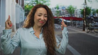 Bir şehir caddesinde eli kolu çapraz olan ve ellerini kaldırmış bir kadın alaycı alaycı bir ifade sergiliyor..