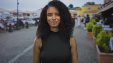 Kıvırcık saçlı İspanyol kadın kamerayı işaret ediyor ve güneş ışığında gülümsüyor. Eğlenceli bir davet..