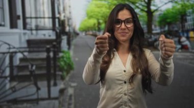 Latin kökenli genç bir kadın, gözlüklü, pandomimci, elleriyle direksiyonu kavrayan, şehir caddesinde gülümseyen, kendine güvenen..