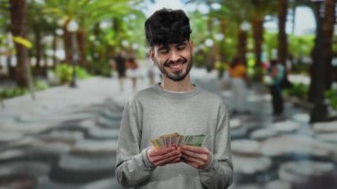 Elinde Norveç Kronu banknotları olan bir adam arka planda palmiye ağaçları olan canlı bir şehir sokağında açık hava finans teması sergiliyor..