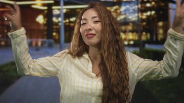 Gece yarısı aydınlık bir şehir binasının önünde iki eliyle barış işareti yapan bir kadın, görünür kırmızı tırnaklar ve uzun saçlar; neşeli bir güven..