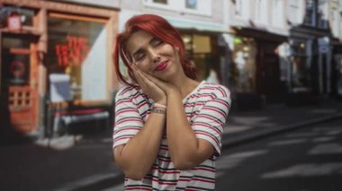 Kadın elleri ve avuç içi yanakları ile dinlenen şehir caddesinde çizgili gömlek ve saat; rüya memnuniyeti.