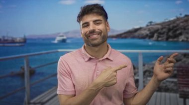 Güneşli bir günde deniz kenarındaki terasta işaret parmağıyla işaret eden İspanyol genç adam..