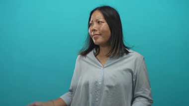 Avuç içleri havada bir kadın turkuaz bir stüdyo ortamında elini gösteriyor, açık düğmeli gömlek ve bilezik takıyor; belirsizlik.