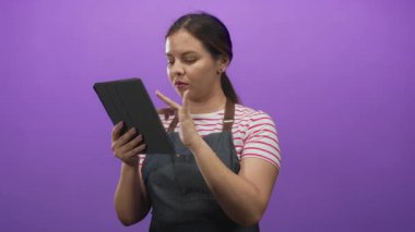 Çizgili gömlek ve kot önlüklü kadın mor stüdyoda sessizlik için parmak dudağa tablet tutuyordu..