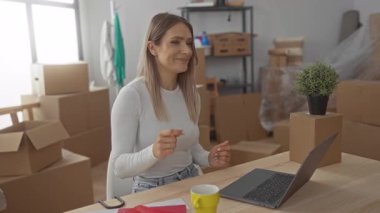 Yeni dairesinde mutlu bir şekilde dans eden genç bir kadın taşınan kutuların arasında yeni yaşam alanına uyum sağlarken mutluluğu ve başarıyı simgeliyor..