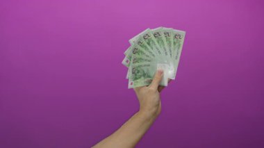 Pembe arka planda tek kişilik banknotlar tutan bir adam fan düzeninde birden fazla banknot gösteriyor, para ve finans kavramlarını vurguluyor..