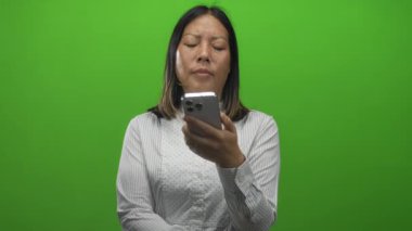 Genç İspanyol kadın akıllı telefon tutuyor, yeşil stüdyoda kaşlarını çatıyor ve parmağını kaldırıyor. Hayal kırıklığı teknolojisi sorunu..