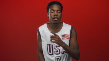 Kırmızı fotoğraf stüdyosunda sessiz kalmak için parmak dudağa ABD forması giyen Afro-Amerikan genç adam..