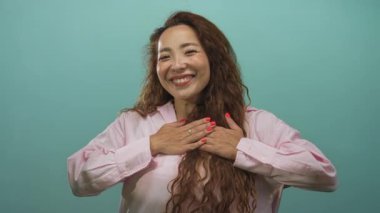 Nane yeşili stüdyoda pembe gömlek giyerek kollarını açmış gülümseyen genç bir kadın..