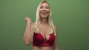 Kırmızı dantelli sutyen giyen sarışın kadın yeşil stüdyoda el sıkışmak için elini uzatıyor ve çıplak göğüs dekoltesini gösteriyor..