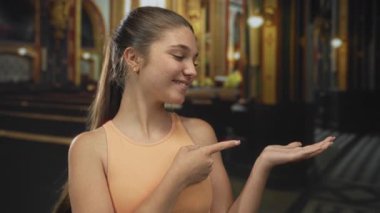 Kafkasyalı genç kız kolsuz üst puanlar giyerek Katolik kilisesinin iç kısımlarındaki sıralar arasında avuçlarını açmak için parmağını uzattı..