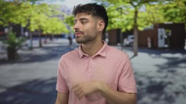 Bulanık bina cephelerinin ortasında pembe bir polo tişört giyen İspanyol genç adam, merak.