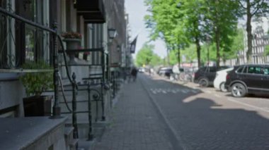 Avrupa sokak sahnesi, güneşli bir gökyüzü altında karakteristik mimari, bisikletler ve kentsel etkinliğin yer aldığı, bokeh efektli odaksız bir görünümü gösteriyor.