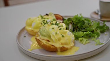 Restoranda taze soğan ve kremalı holandez sosunun ön plana çıkarıldığı bir tabakta yemyeşil salata ile yumurtalı kahvaltı sahnesi..
