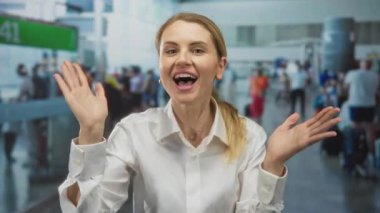 Kapalı alanda hareketli hareketler yapan, beyaz gömlekli, bulanık kalabalıkla çevrili, muhtemelen bağıran, yoğun seyahat sahnesini anımsatan, aciliyet ve bağlantı kuran bir kadın..