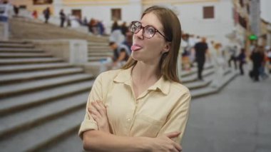 Kolları çapraz ve dili sokak basamaklarında sallanan, gözlüklü ve bej gömlekli bir kadın..